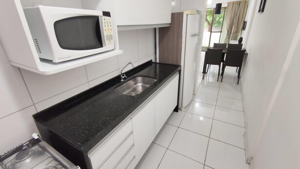 A compact kitchen with a microwave, sink, and stove. - Cohost Apt Praia 101a 80m do mar e 250m da Vila (Ipojuca)