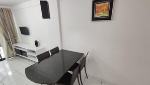 A dining area with a black table and chairs, a white wall, a framed picture, and a TV on a white stand. - Cohost Apt Praia 101a 80m do mar e 250m da Vila (Ipojuca)