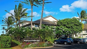 A hotel with a sign reading "Regency at Poipu Kai," surrounded by lush greenery and palm trees. - 5 Beds Downstairs Corner Unit with AC, 3 Pools, 6 minutes to Beaches, Beach Cart (Koloa)