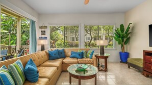A spacious living room with a beige sectional sofa, a glass coffee table, and a ceiling fan. - 5 Beds Downstairs Corner Unit with AC, 3 Pools, 6 minutes to Beaches, Beach Cart (Koloa)