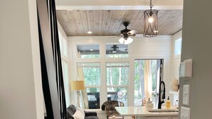 A spacious living room with a dark sofa, a wooden coffee table, and a large window offering a view of the outdoors. - Eagle’s Nest Tiny House: Cozy Escape w/ Porch, Patio + Fire Pit (Tracy)