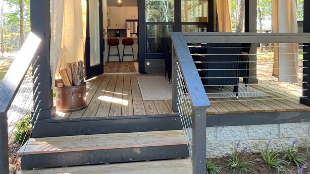 A covered outdoor area with a wooden deck, a ceiling fan, and a view of the backyard. - Eagle’s Nest Tiny House: Cozy Escape w/ Porch, Patio + Fire Pit (Tracy)