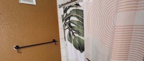 Een badkamer met een bruine wand, een witte douchegordijn met bladmotieven, een witte badkuip en een marmeren vloer.