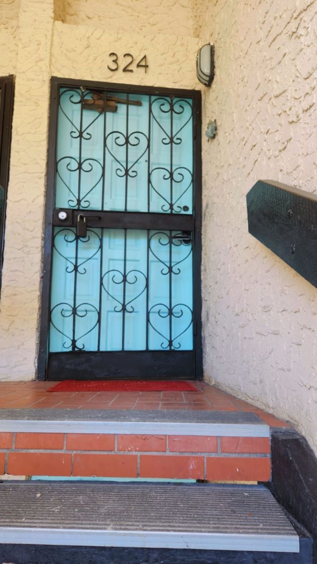 Entrada de un edificio con una puerta numerada, un felpudo rojo y un escalón de ladrillo.