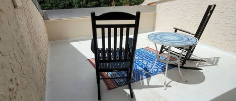 Un balcon avec une chaise noire et une petite table ronde recouverte d’une nappe à motifs.