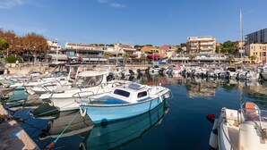 A marina with boats docked, buildings in the background, and clear skies.