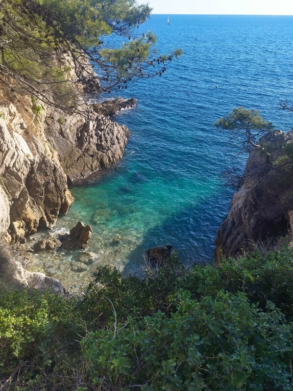 A coastal landscape with rocky cliffs, clear blue sea, and sparse vegetation.