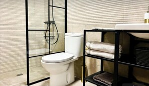 A modern bathroom with a toilet, a glass-enclosed shower, and a shelf with towels.