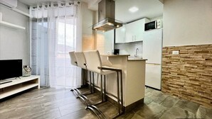 A compact kitchen with a microwave, a stove, and a bar area with stools. - Vacation Apartment 'Relaxing Los Cristianos' with Sea View, Wi-Fi and Air Conditioning (Los Cristianos)