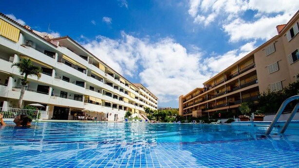 A swimming pool with tiled flooring, surrounded by multi-story buildings with balconies. - Vacation Apartment 'Relaxing Los Cristianos' with Sea View, Wi-Fi and Air Conditioning (Los Cristianos)