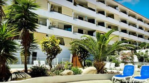 Un hôtel à plusieurs étages doté de balcons, d’un espace piscine avec des chaises longues et d’un aménagement paysager de style tropical.
