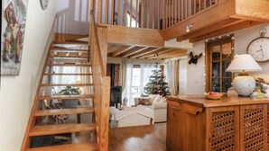 Eine Holztreppe führt zu einem Schlafzimmer mit Erker, einer Deckenleuchte, einem Weihnachtsbaum und einem Essbereich mit einer Lampe.