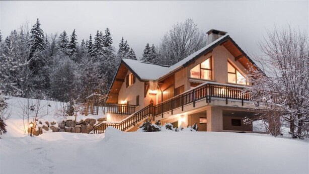 Ein großes, mehrstöckiges Holzhaus mit Balkon, umgeben von schneebedeckten Bäumen.