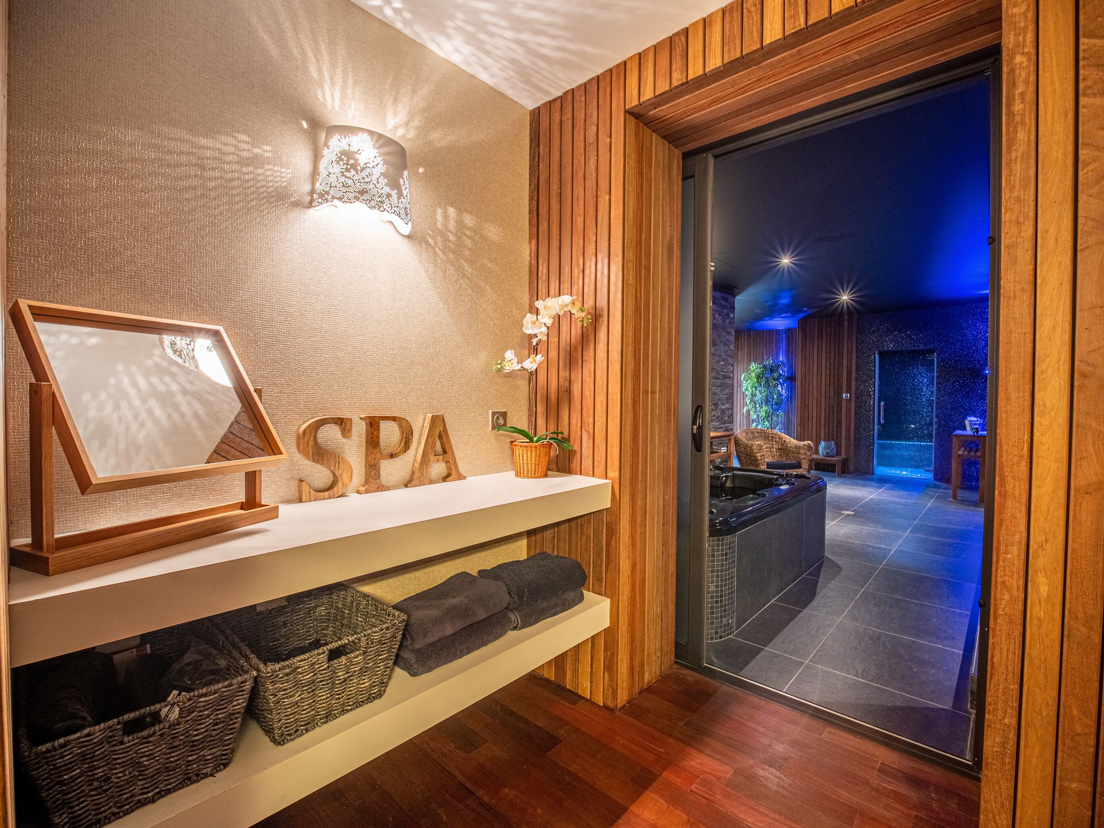 Un espace spa avec un lambris en bois, un tableau encadré, une enseigne indiquant « SPA », un luminaire fixé au mur et un aperçu d’un jacuzzi.