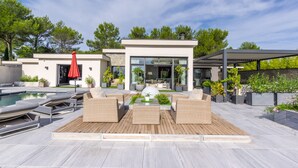 Un espacio exterior moderno con piscina, sillones de descanso y un porche cubierto.