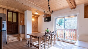A wooden interior with a dining table, chairs, a sofa, a TV, and a sliding glass door to the outside.