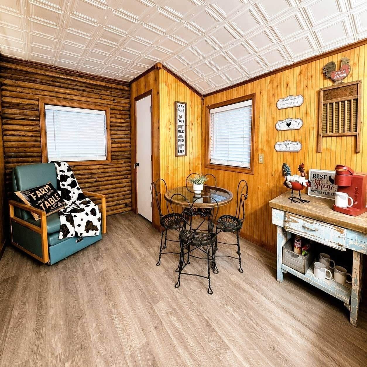 A cozy room with a wooden interior, a dining table with chairs, a coffee station, and a window with blinds.