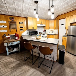 A kitchen with wooden cabinets, a central island, bar stools, a microwave, a stove, and a refrigerator.