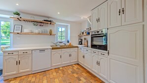 Une cuisine avec des meubles blancs, un lave-vaisselle, un four et une fenêtre donnant sur un paysage verdoyant.