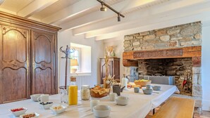 Une table de petit-déjeuner installée près d’une cheminée en pierre, avec des meubles en bois et une longue table sur laquelle sont disposés des bols et divers aliments pour le petit-déjeuner.