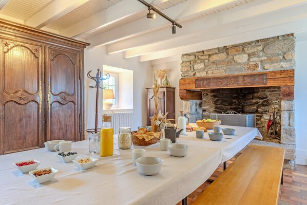Una mesa larga con tazones y alimentos para el desayuno, junto a una chimenea de piedra y armarios de madera.