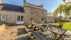 Un bâtiment en pierre avec un toit en tuiles, des tables de pique-nique en bois et une cour gazonnée.