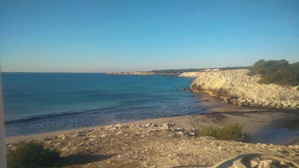 Eine Küstenlandschaft mit einem felsigen Strand, ruhiger See und einem fernen Leuchtturm.
