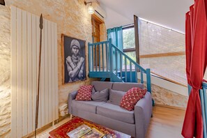 A room with a grey sofa, a staircase with blue railings, a framed picture on the wall, and a window with a view. - Scarabée Guest Room – Elegance and Serenity with Shared Pool and Air Conditioning (Sarlat-la-Canéda)
