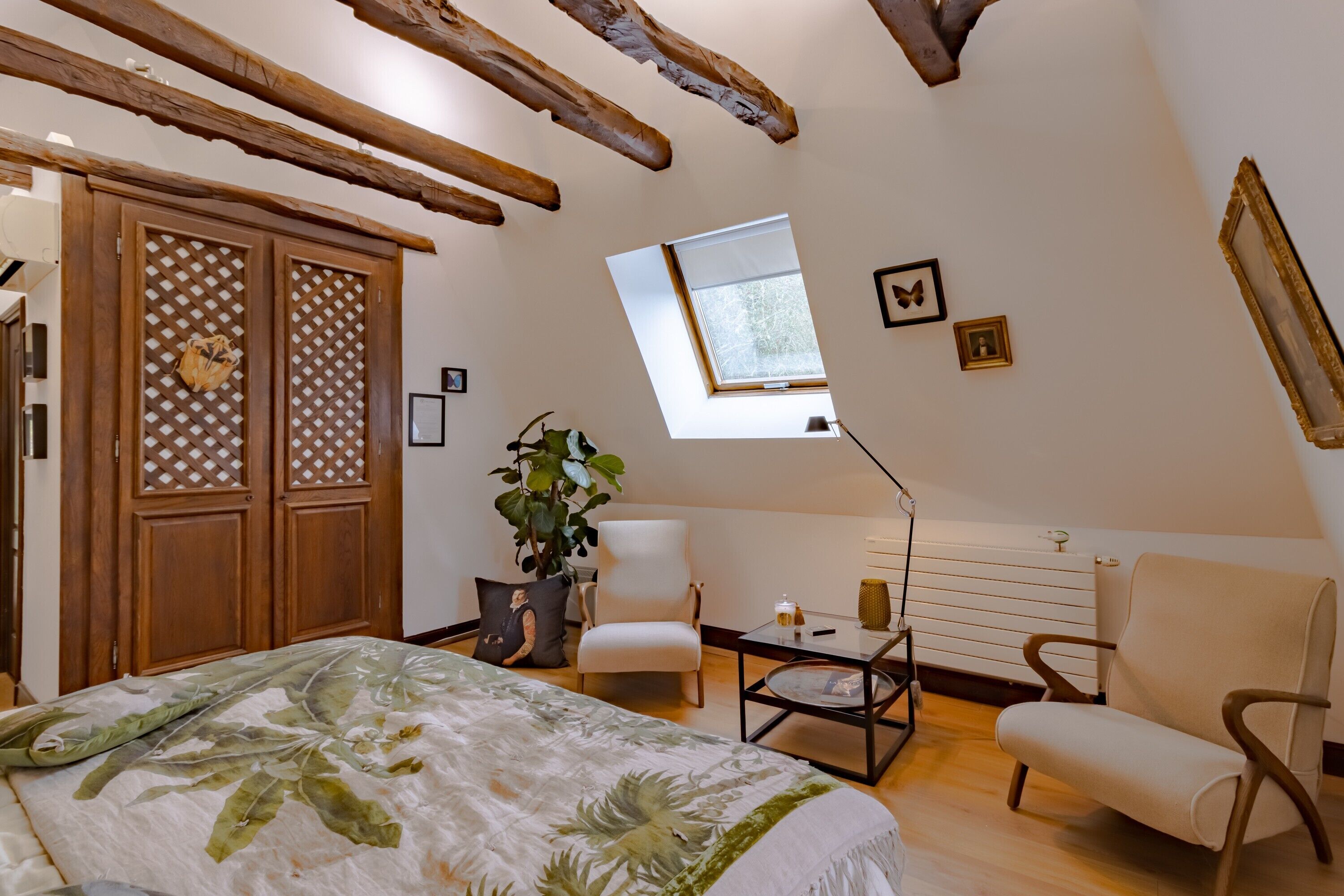 Une chambre à coucher avec un lit, une chaise, une table, une fenêtre et des poutres en bois au plafond.