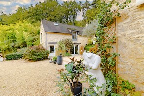 A stone house with a gravel driveway, potted plants, and a statue.