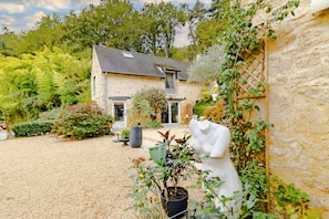 A stone house with a gravel driveway, potted plants, and a statue.