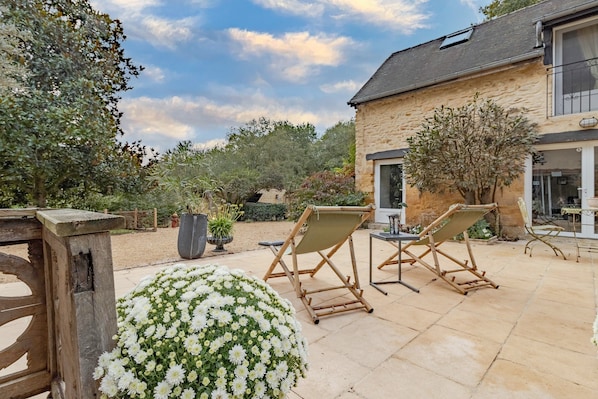 A stone building with a patio, two folding chairs, and a large flower arrangement.
