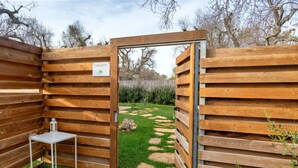 Une porte en bois avec une pancarte, une petite table et un chemin de pierres menant à une zone herbeuse.