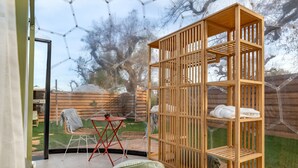 Une pièce avec une étagère en bois, une petite table entourée de chaises et une vue sur un jardin avec une clôture en bois et des arbres.