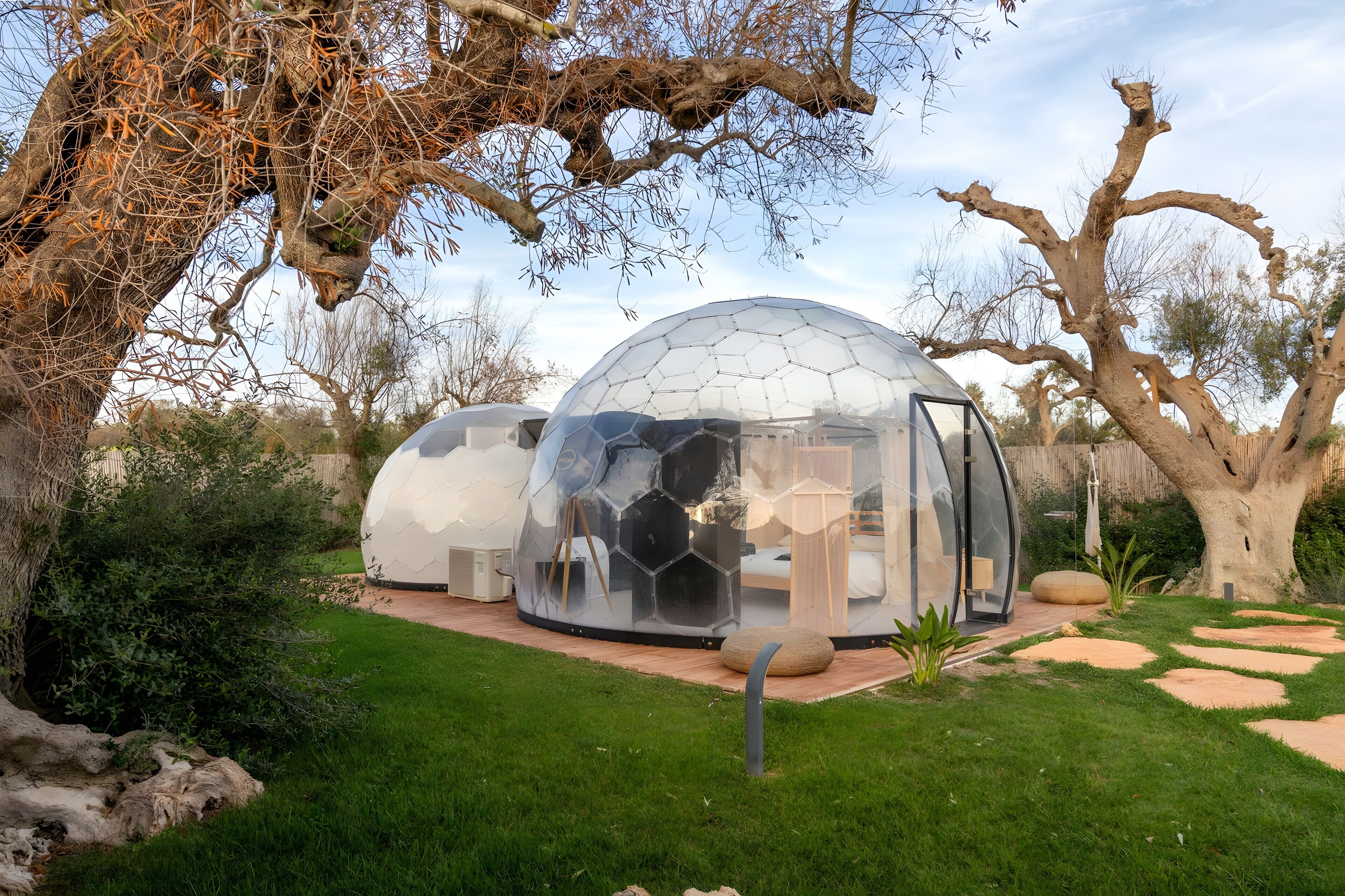 Dos estructuras en forma de cúpula transparente con interiores de madera, rodeadas de césped y árboles.