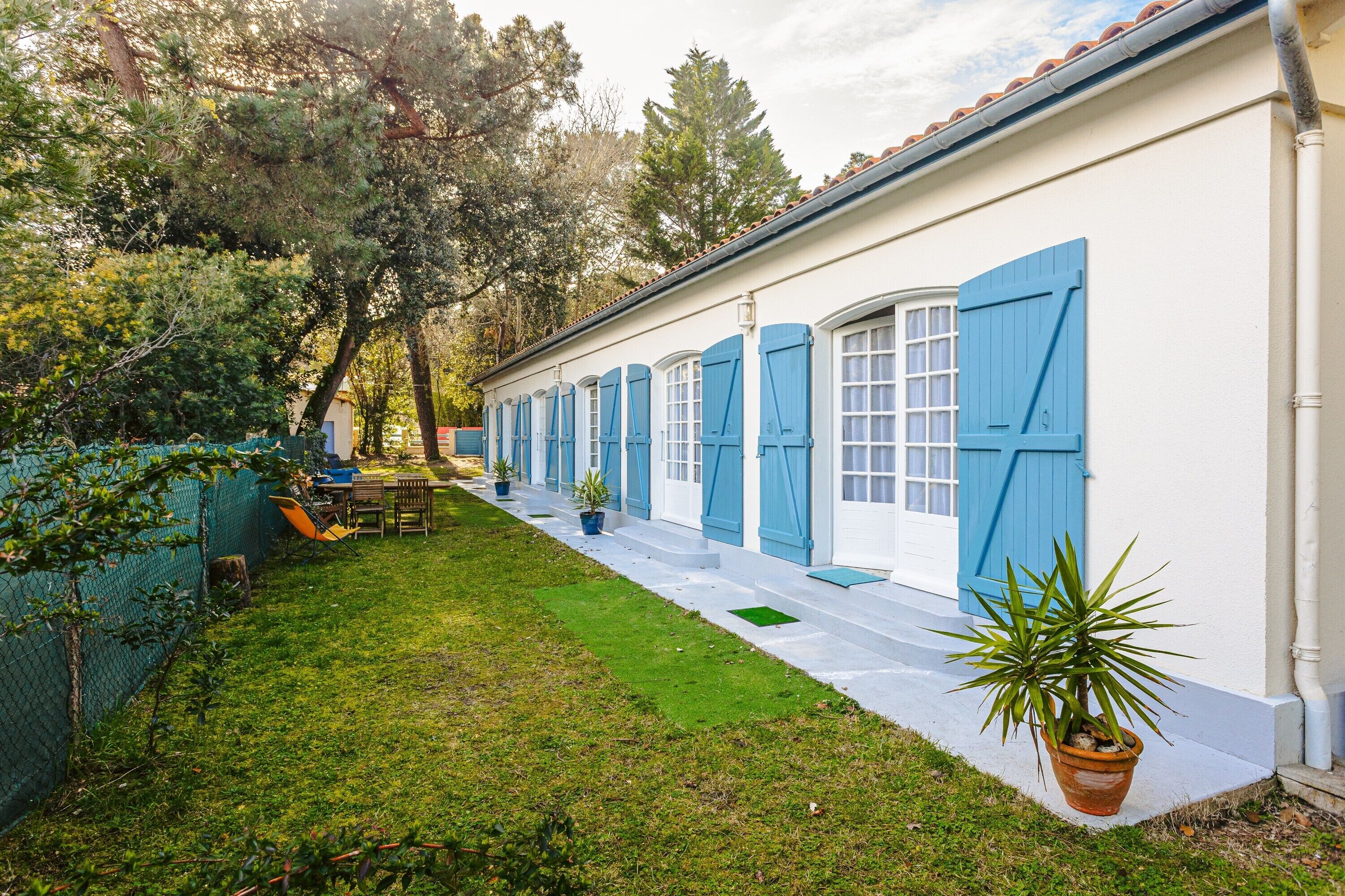 Un bâtiment blanc avec des volets bleus, une pelouse verte et une plante en pot.
