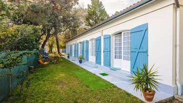 Un bâtiment blanc avec des volets bleus, une pelouse verte et une plante en pot.