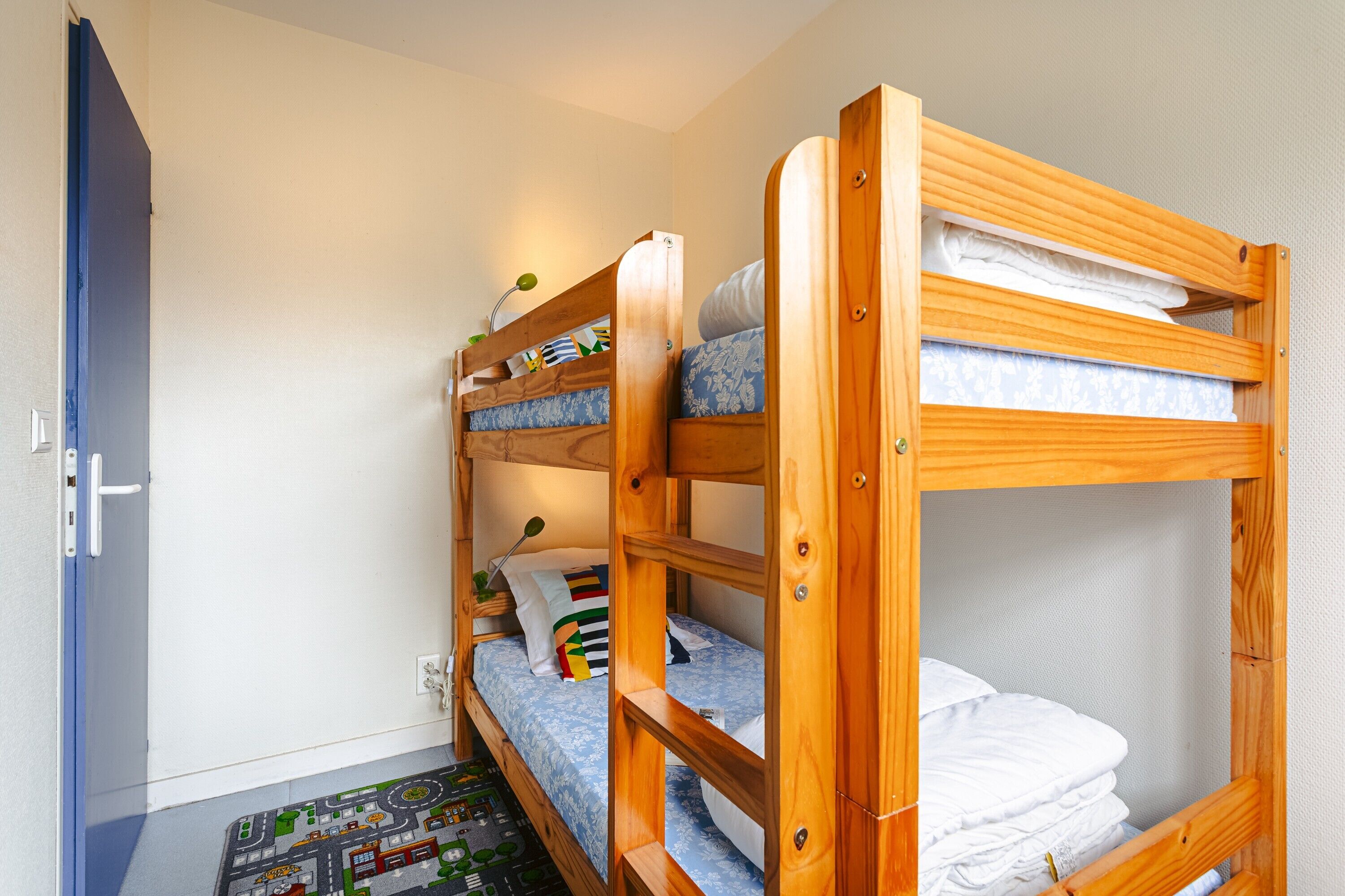 Habitación con literas, un tapete con motivos de la ciudad, una puerta y una pared con interruptor de luz.