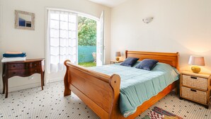 A bedroom with a wooden bed, a bedside table, a lamp, a small cabinet, and a door leading to a balcony.
