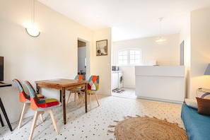 Un espace de vie compact comprenant un coin repas, une cuisine et un petit coin salon avec un canapé et un tapis rond.