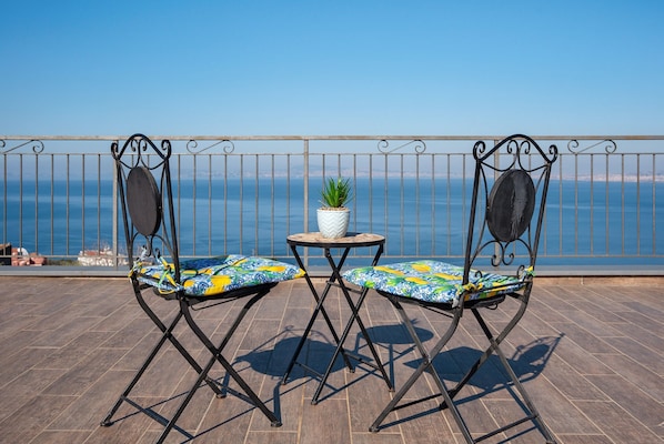 A balcony with two chairs and a small table, a potted plant, and a view of the sea.