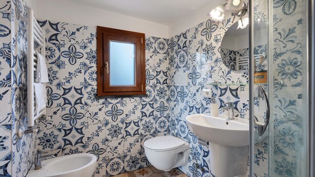Une salle de bain comprenant des toilettes, un bidet et un lavabo, le tout orné de carreaux aux motifs floraux bleus.