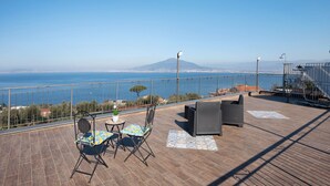 Une terrasse offrant une vue sur la mer et les montagnes, aménagée avec des chaises et une table.