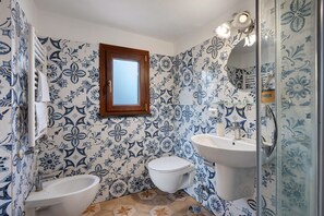 Et badeværelse med toilet, bidet og vask, alt sammen med blå blomstermønstre.