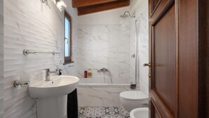 Ein Badezimmer mit Marmorwand, Waschbecken, Badewanne und Toilette.