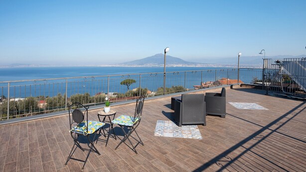 Eine Terrasse mit Blick auf das Meer und ein Berg, möbliert mit Stühlen und einem Tisch.