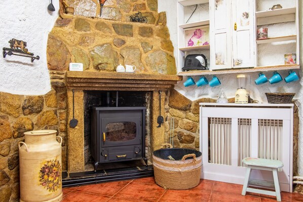 A stone fireplace with a black stove, a white cabinet with blue mugs, and a wicker basket.