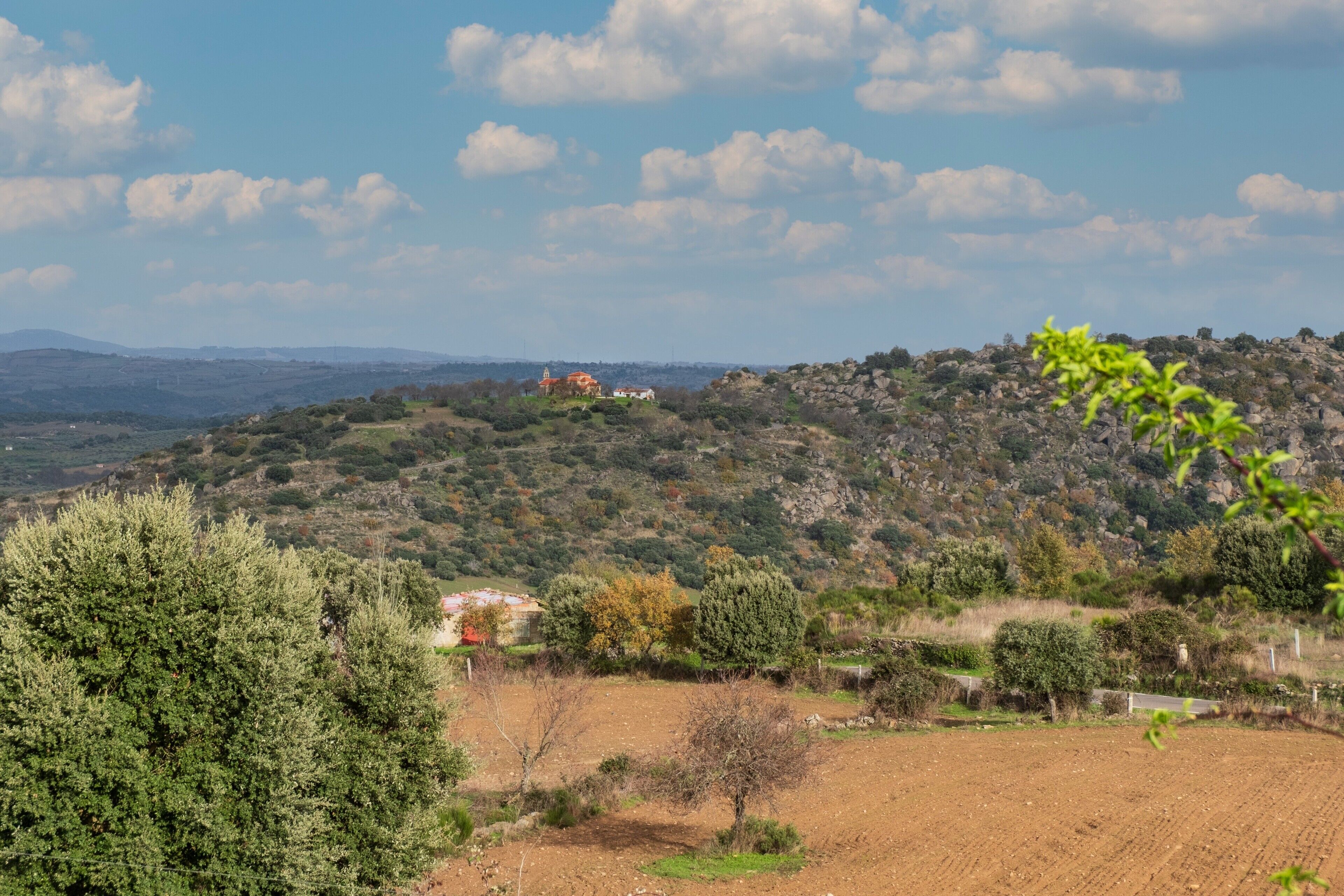 A rural landscape with a building on a hill, surrounded by trees and open fields.