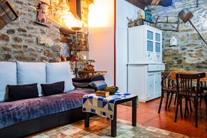 A cozy room with a stone wall, a wooden sofa, a small table with a quilt, and a dining area with chairs and a table.