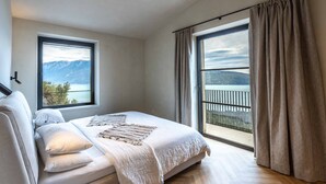 Ein Schlafzimmer mit einem großen Bett, zwei Fenstern, Bergblick und einem Balkon.